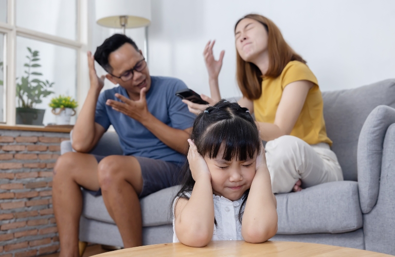 Sad little girl closes her ears while her parent are having a fight