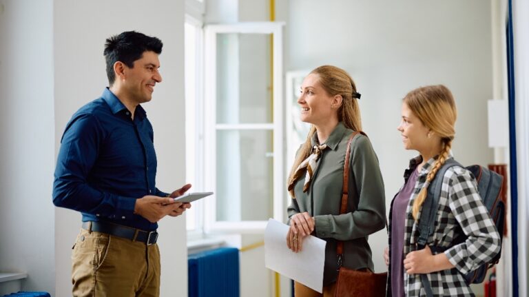 Happy principal talking to mother and daughter about enrolling in high school