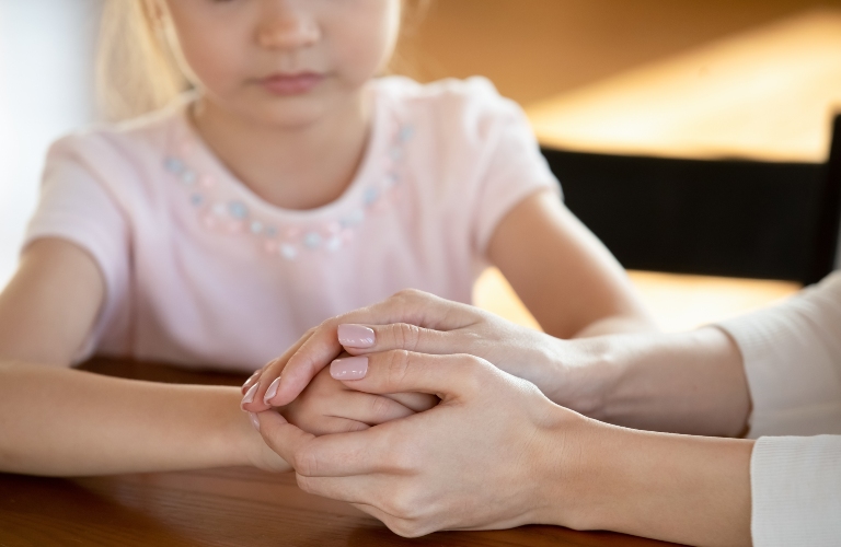 Focus on young woman holding hands of sad small preschool girl