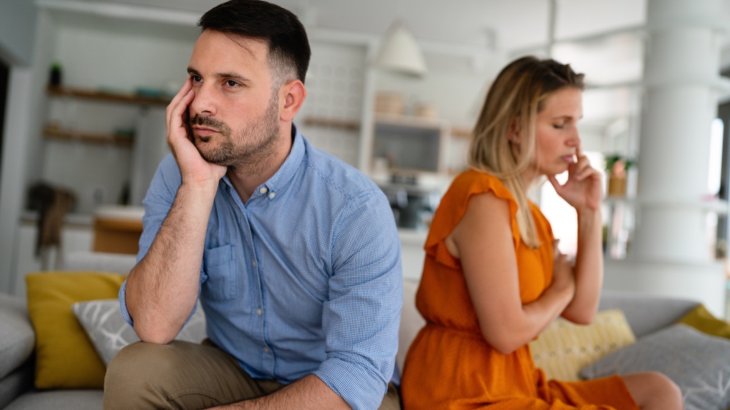 Sad pensive couple thinking of relationships problems sitting on sofa, conflicts in marriage